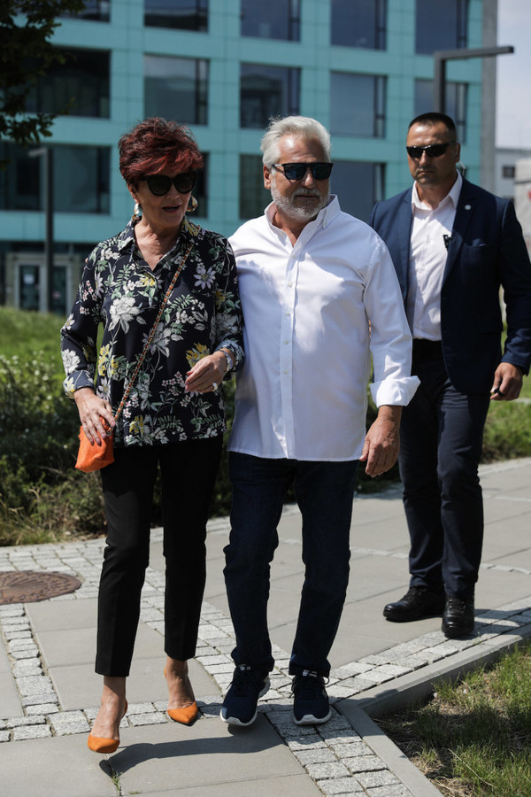 Jolanta Kwaśniewska w kwiecistej koszuli, ciemnych spodniach i pomarańczowej torebce. Buty dobrała pod kolor torebki.  