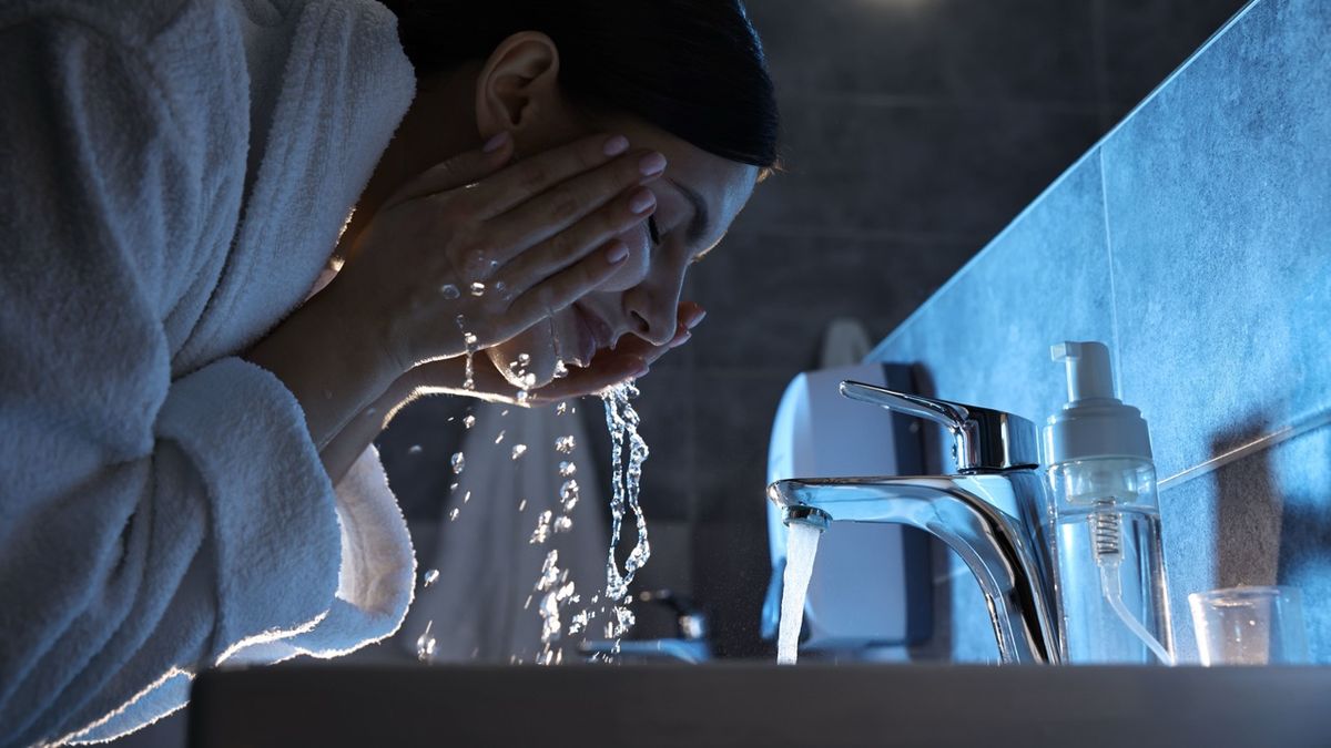 Woman washing her face over sink in bathroom