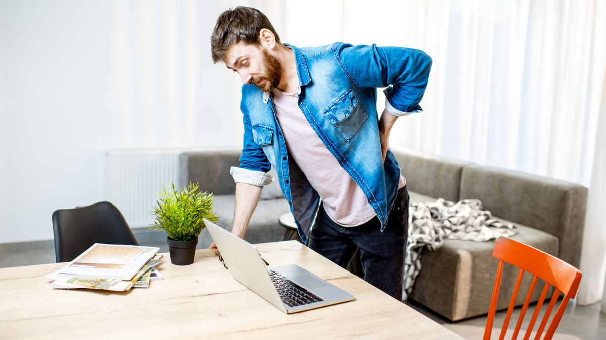 Man suffering from acute back pain while standing up from the working place at home