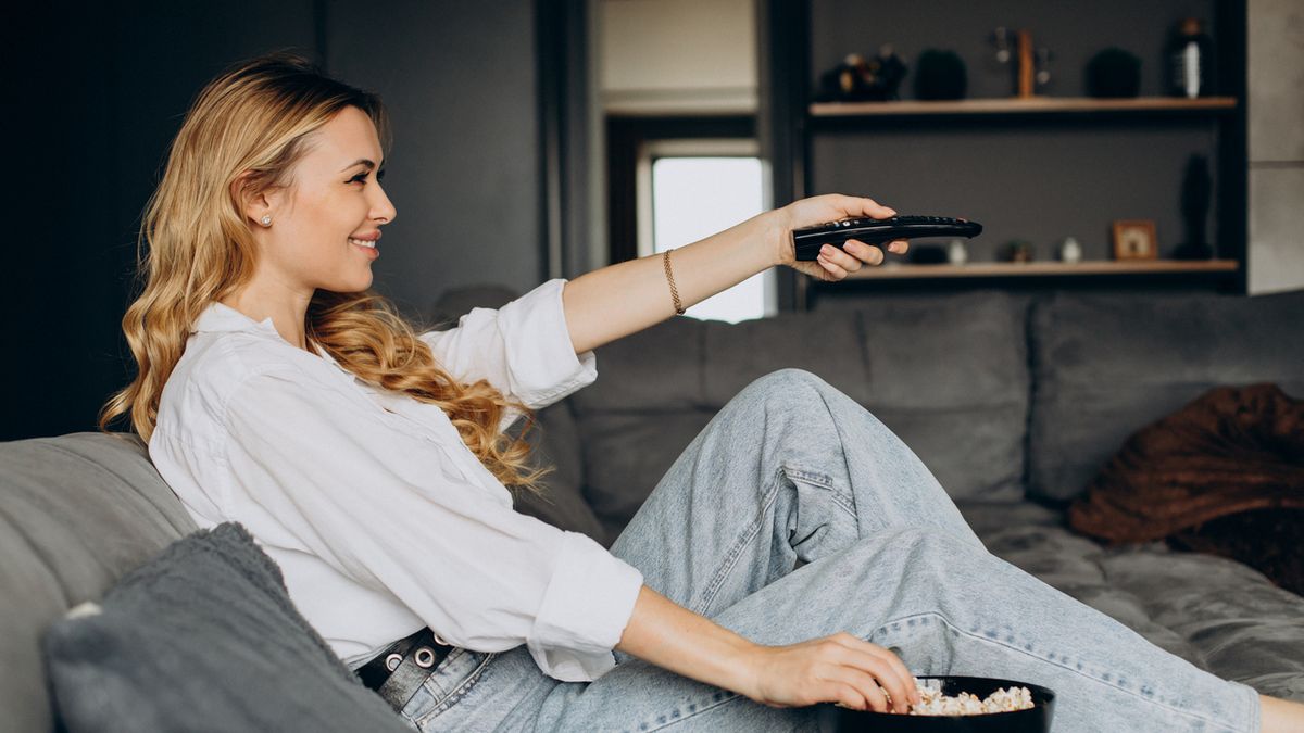 Woman eating popcorn at home on couch and watching movie