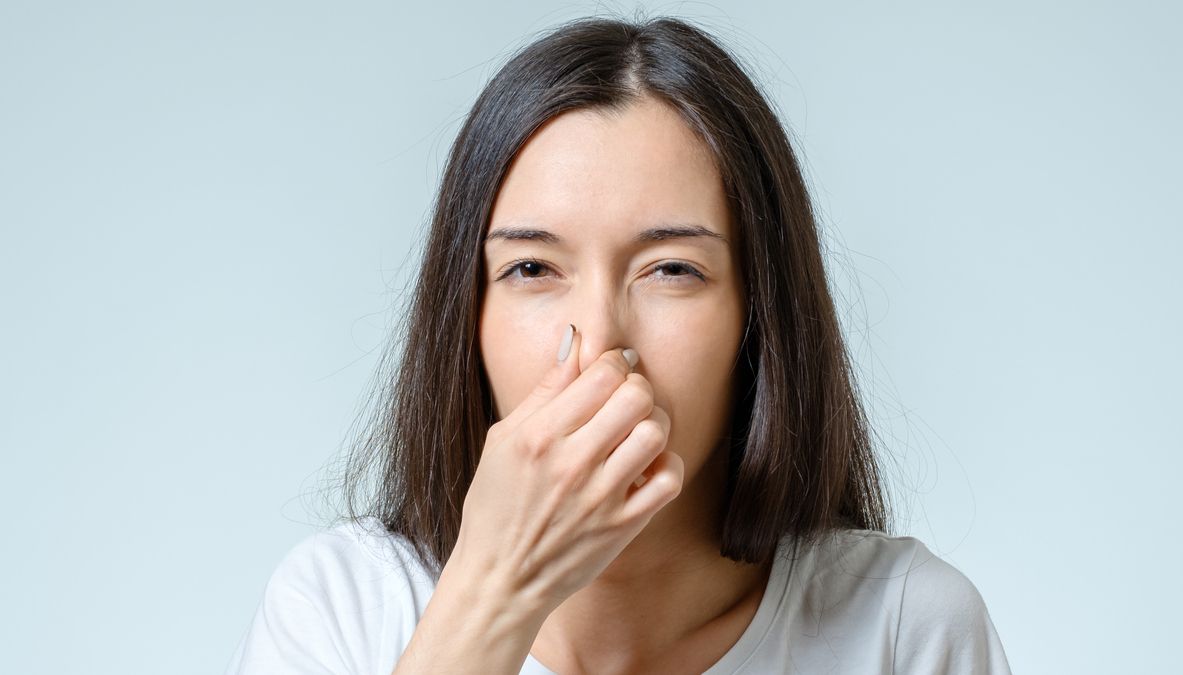 Girl covers nose with hand showing that something stinks isolated on gray background