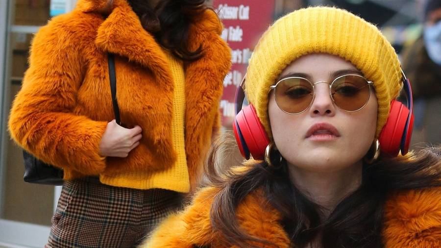 Selena Gomez w pomarańczowym futerku na planie filmu.