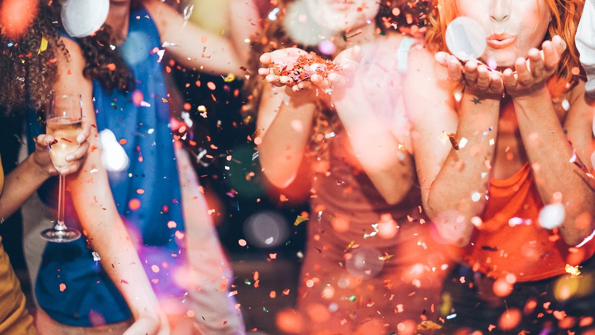 Happy friends making carnival party throwing confetti - Young people celebrating on weekend night - Entertainment, fun, nightlife and fest concept - Focus on center girl hands