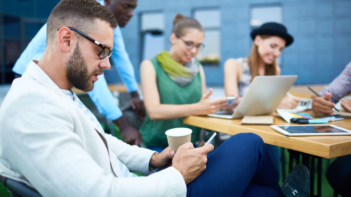 Modern businessman with smartphone on background of working designers