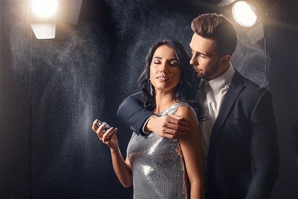 Stylish young couple with perfume on dark background