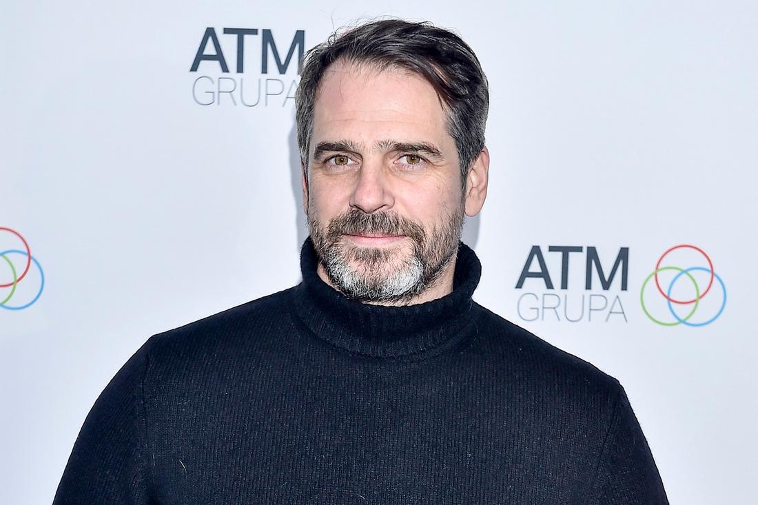 Paweł Deląg w czarnym golfie na ściance. 