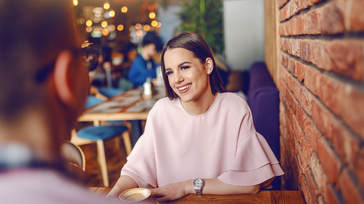 Beautiful young brunette sitting in cafeteria, drinking coffee and flirting with her boyfriend.