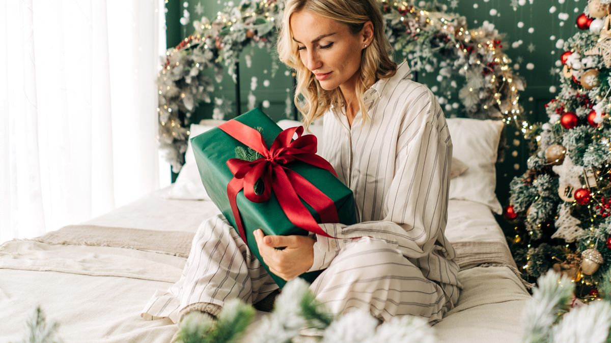 Attractive happy woman sitting on bed in christmas time opens gift boxes